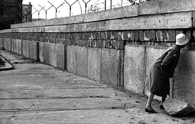 Woman looking through a hole in the Berlin Wall.