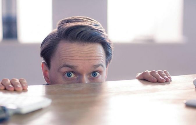 Nervous businessman peeking over desk in his office